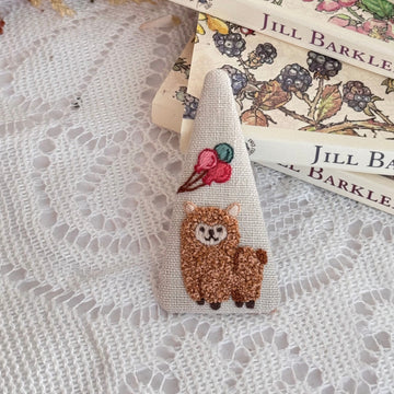 Embroidered ribbon with a llama design on a textured surface with books in the background