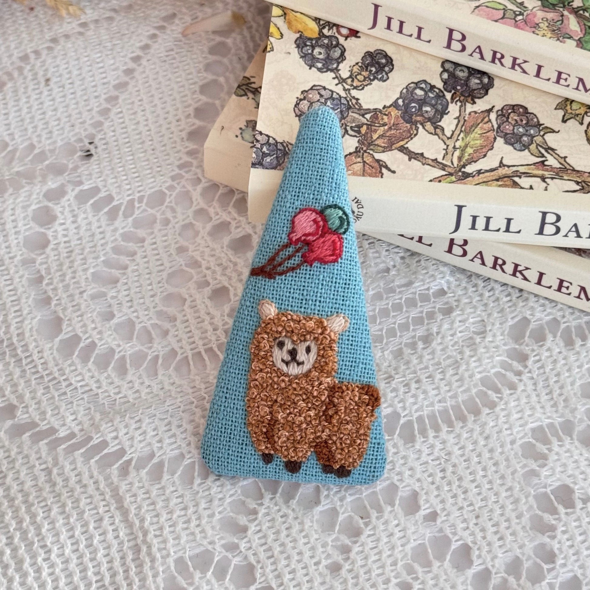 Embroidered bear pin on a stack of books with floral designs