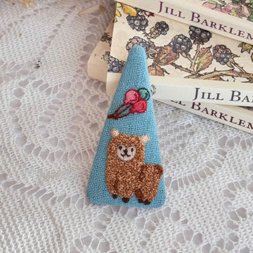 Embroidered bear pin on a stack of books with floral designs