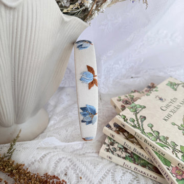 Floral-patterned knife handle next to a white teapot and books on a lace surface
