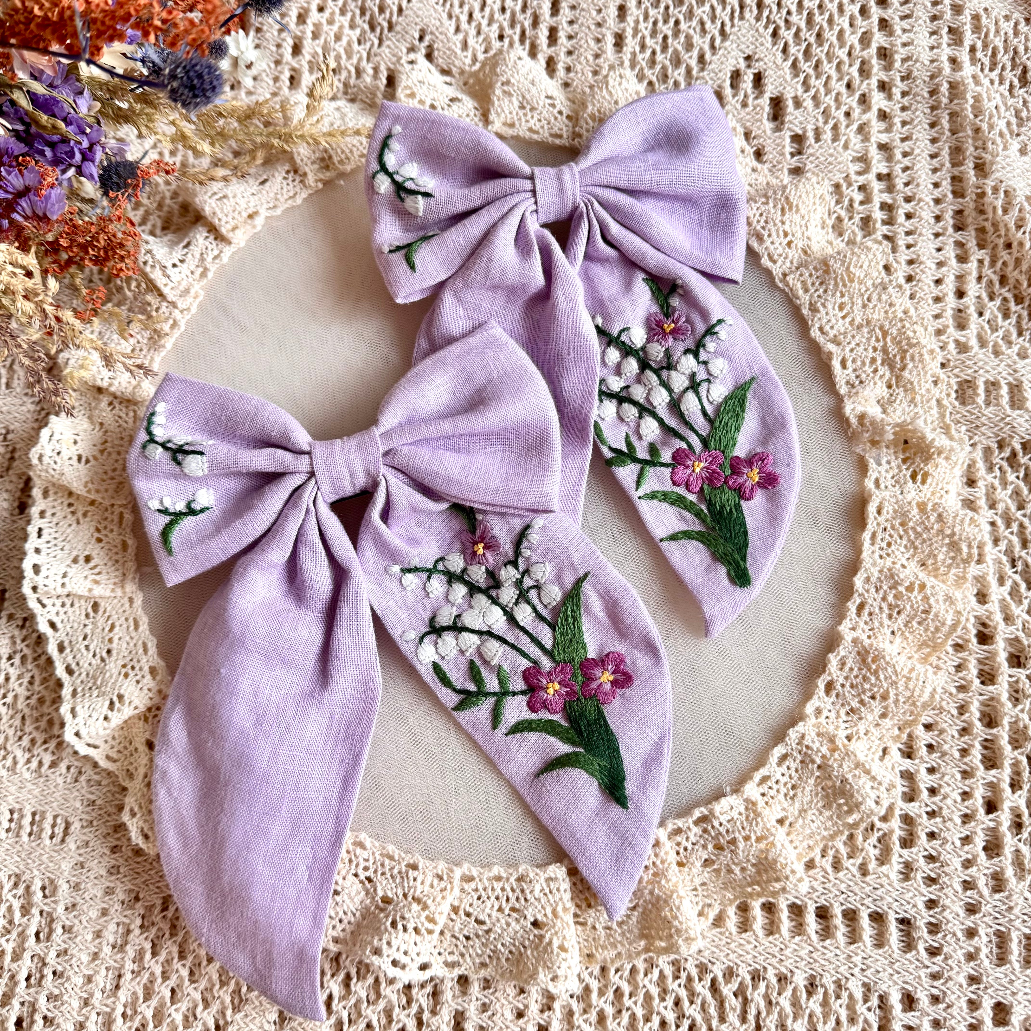 Käsin kirjottu hiusrusetti, kielo ja luhtalemmikki -aiheinen kuvio kankaalla