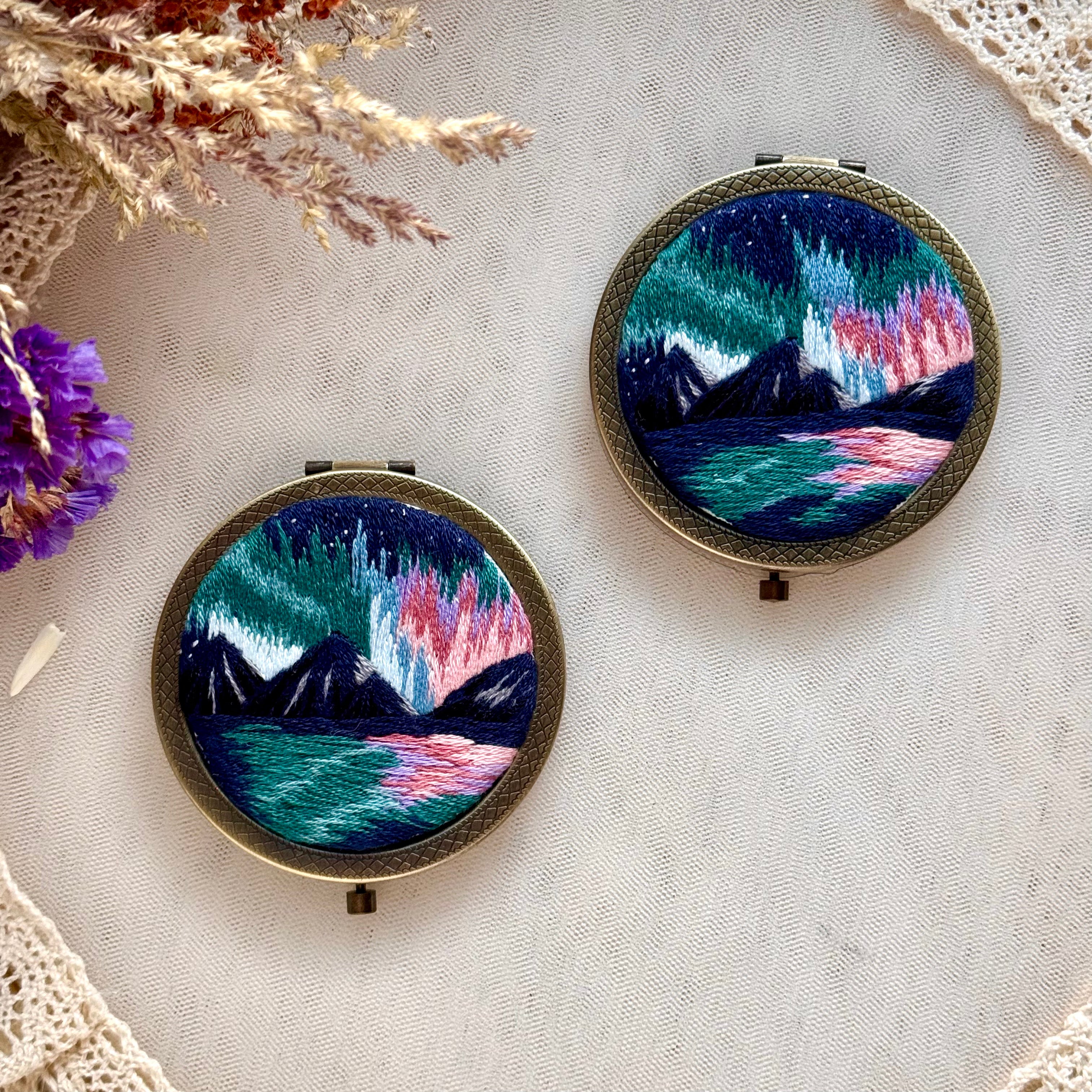 Käsin kirjottu taskupeili, revontulet-aiheinen kuvio kannessa