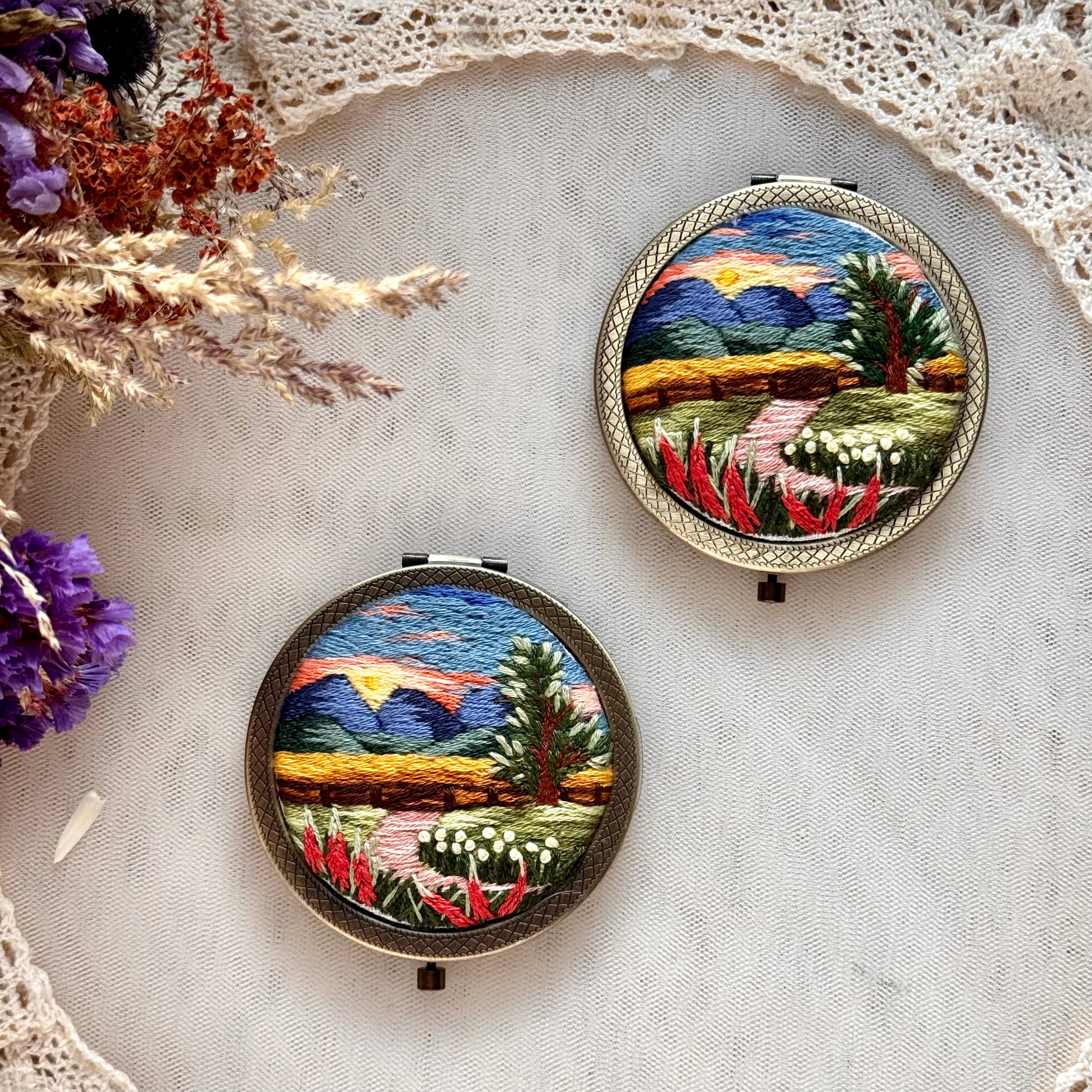 Käsin kirjottu taskupeili, syksyinen auringonlasku -aiheinen kuvio kannessa