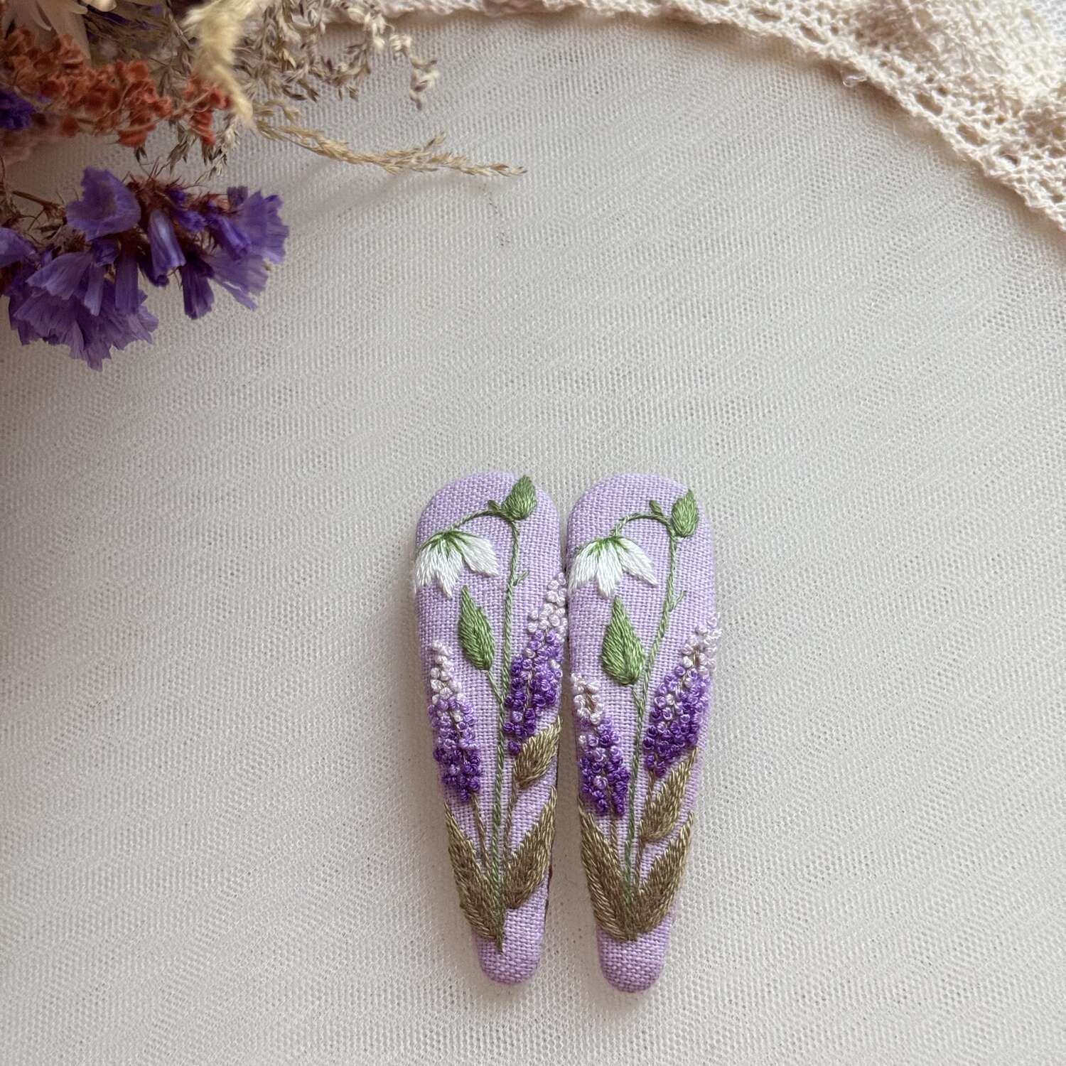 Käsin kirjotut hiuspinnit, vanamo ja syreeni -aiheinen kuvio kankaalla